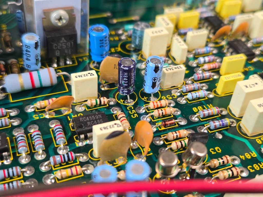 A close-up view of two electrolytic capacitors on the circuit board, one is newer than the other showing the evidence of repair.
