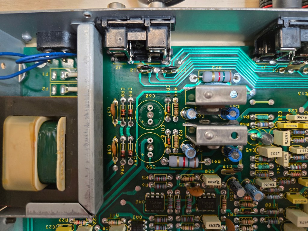 A close up view of the power supply section of the equalizer, with the two main capacitors removed, revealing a ring of fluid leakage beneath one confirming evidence of the failure.