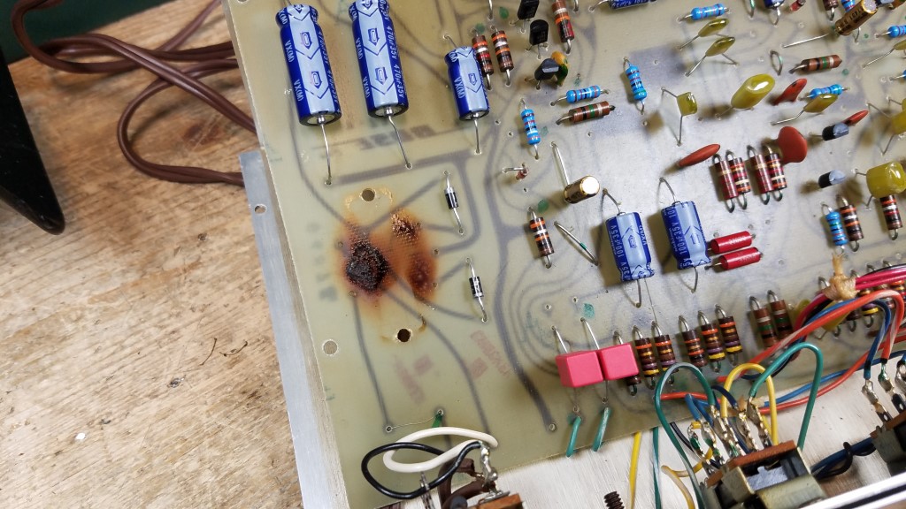 A picture of the circuit board with the power transformer removed, showing large highly visible burn marks where the board was damaged and the transformer destroyed by running it on 240V power when it should have been run on 120V power.