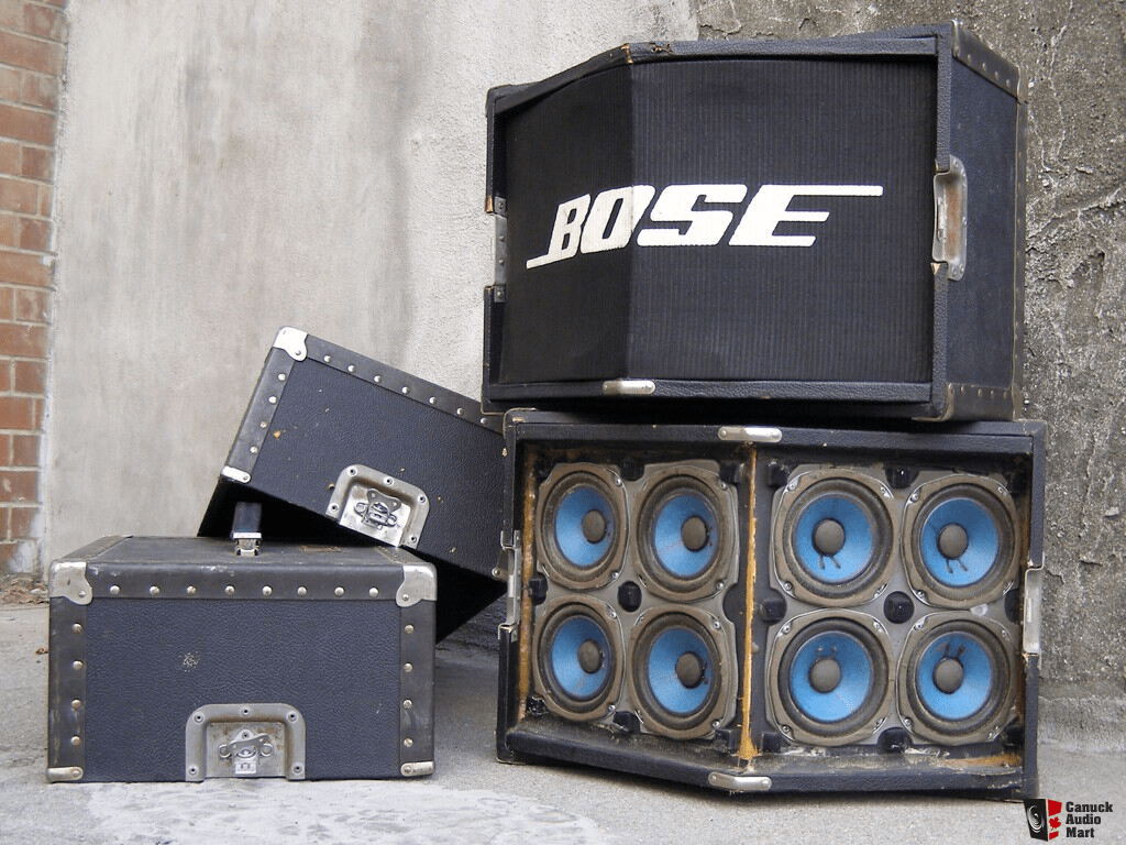 A decorative arrangement of a set of Bose 800 Professional PA speakers, with road cases, and one grille removed to reveal the 8 drivers on the front with blue paper surrounds.