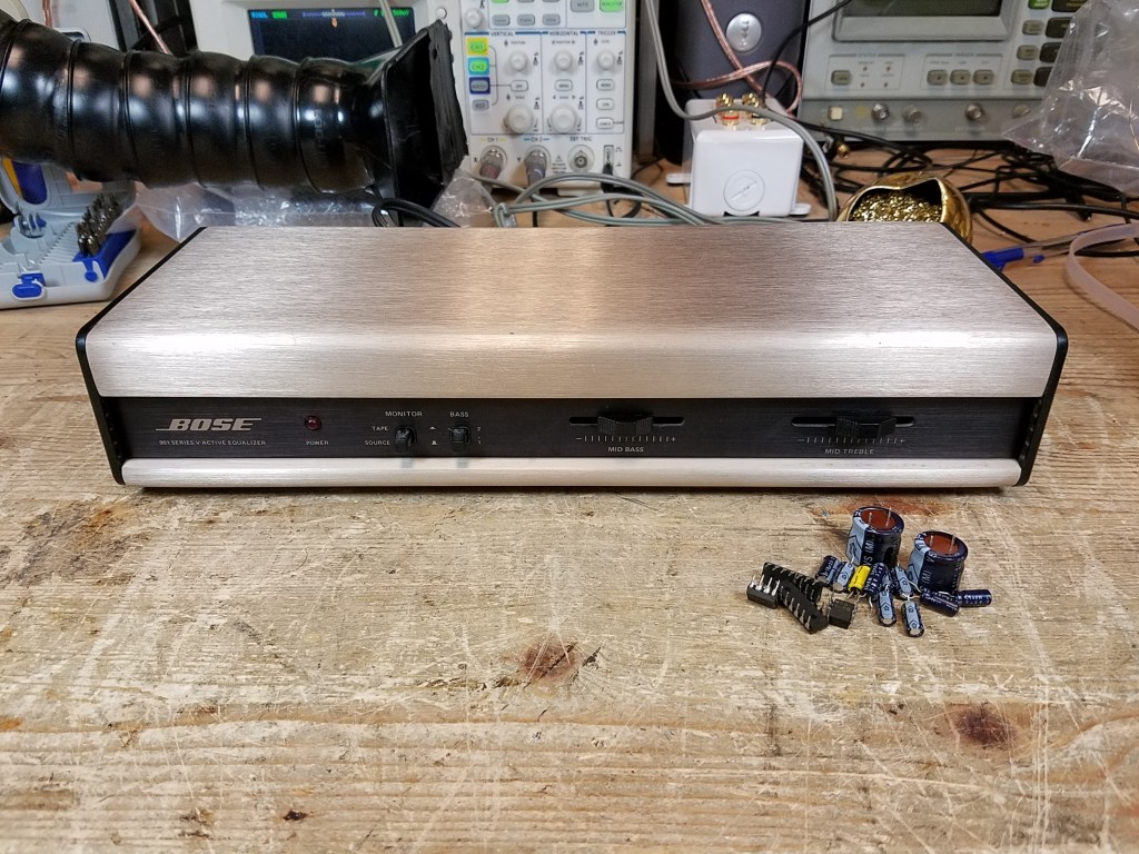 A front view of an equalizer showing the pile of replaced parts sitting in front of it on the workbench.